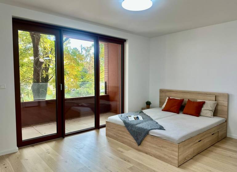 1-bedroom apartment with large windows, wood-patterned flooring, a balcony, and a bed.