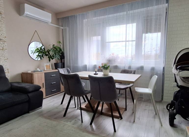 Living room with a gray sofa, wood-decor table, and light curtains in a 3-room apartment.