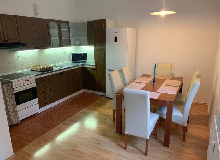 A kitchen in a 2-room apartment with a table, wooden cabinets, and a floor with a wood decor.