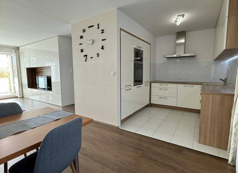 Dining area in a 4-room apartment with a wood-patterned floor and a kitchen in the background.