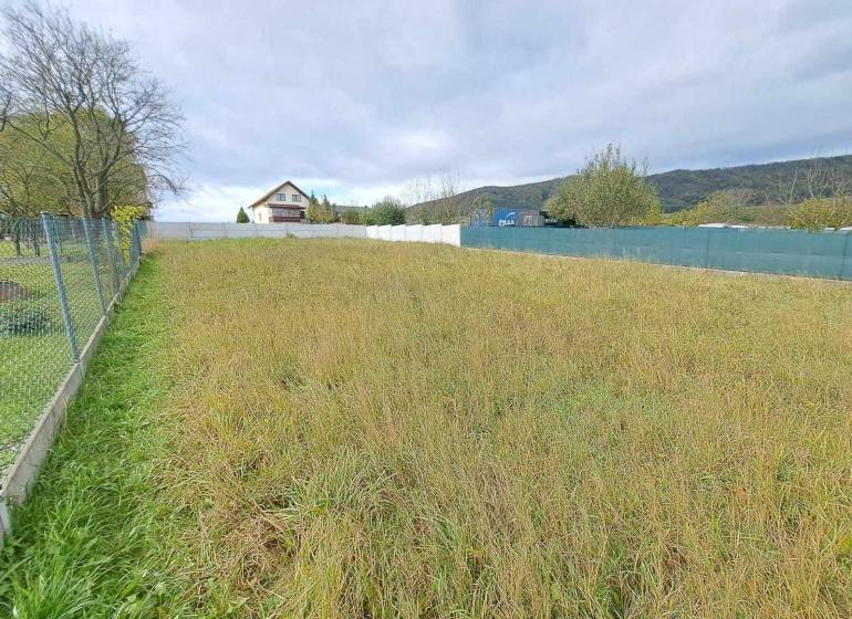 A plot of land with grass, trees, suitable for living, fenced, house in the background.