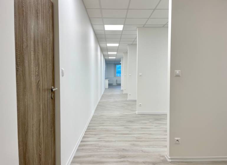 A hallway in an office with white walls, lights, and a wooden decor floor.