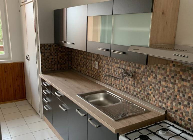 A kitchen in a 2-room apartment with dark furniture and tiled backsplash.