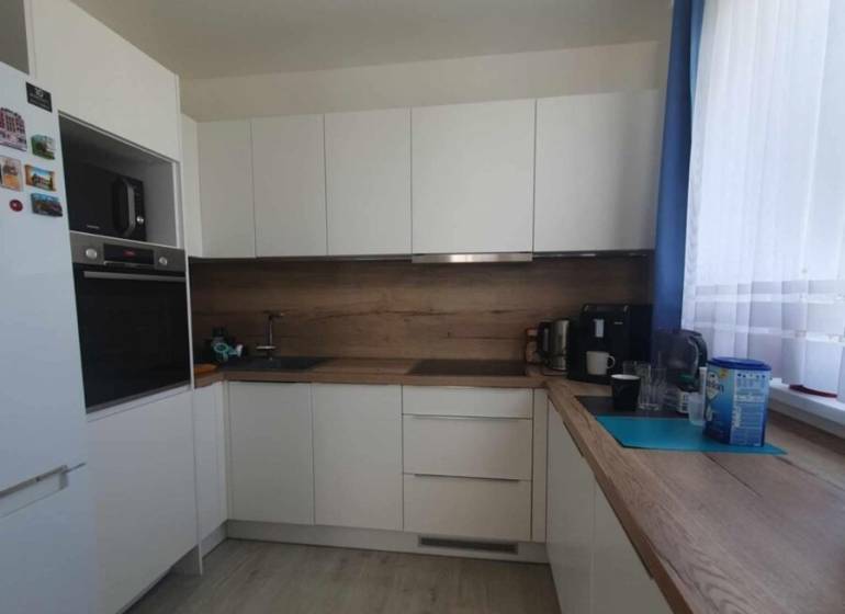 A kitchen with white cabinets, wooden decor on the floor, and a countertop in a 2-room apartment.