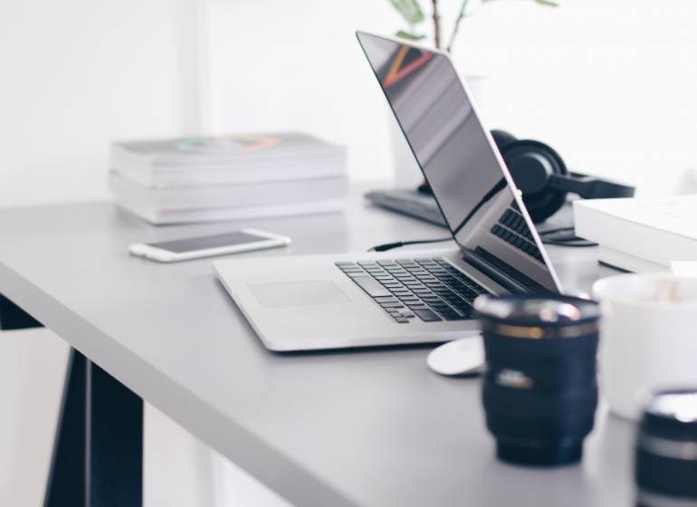 A laptop on the desk in an office with books and a mug.