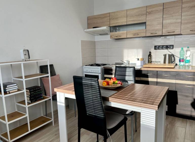 A kitchen in a studio apartment with a wooden decor, a dining table, and a bookshelf.