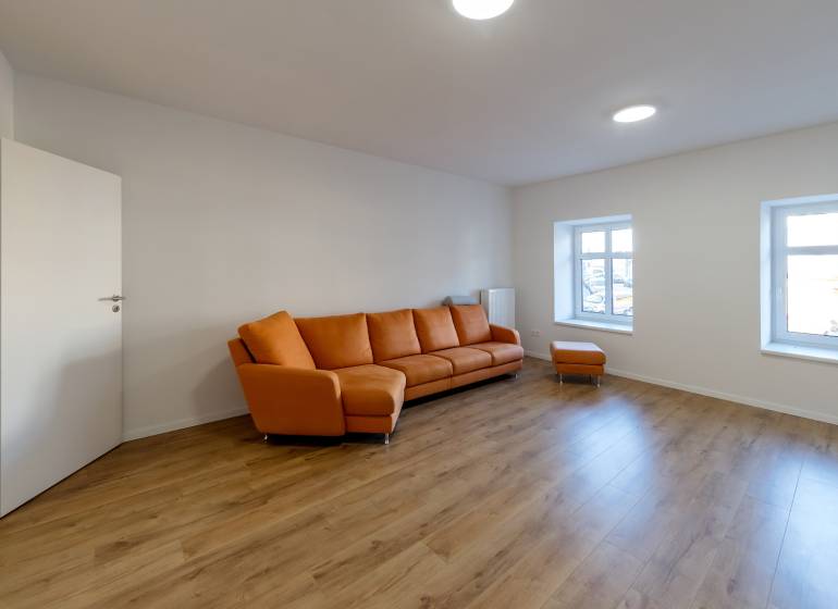 Living room with an orange sofa and a wooden decor floor in a two-room apartment.