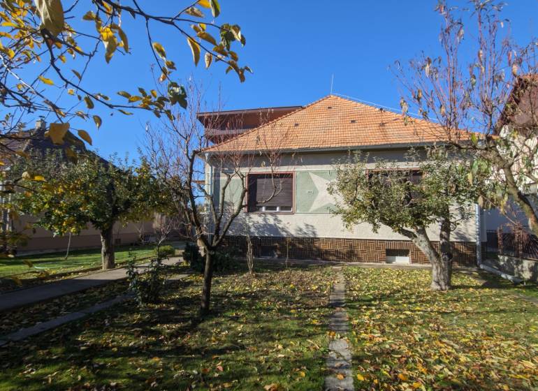 A family house in Vráble with a landscaped garden, bordered by fruit trees in the autumn season.