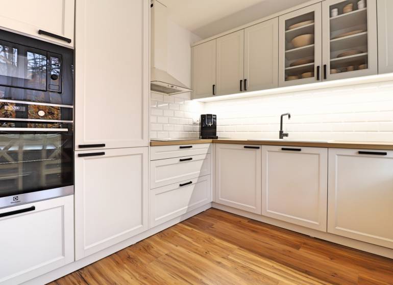 A kitchen in a 3-room apartment with white cabinets and a wooden decor floor.