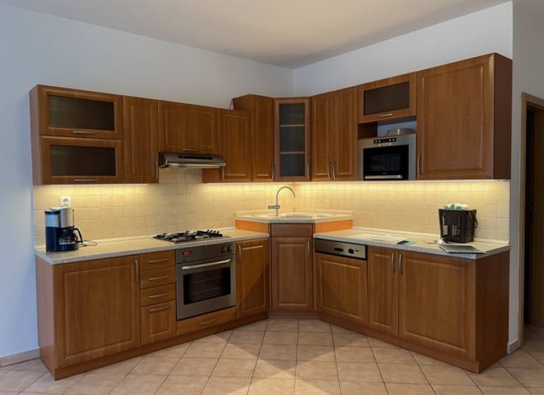 A kitchen unit in a 3-room apartment with wooden cabinets and appliances, light brown tiles.