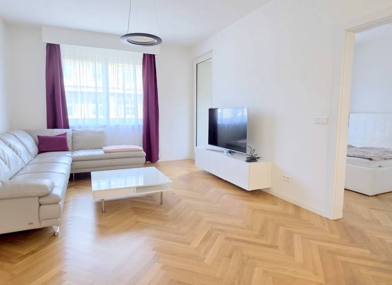 A bright living room in a two-room apartment with a wooden decor floor and a corner sofa.