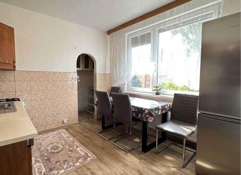A kitchen in a studio apartment with a wood-patterned floor, large window, refrigerator.