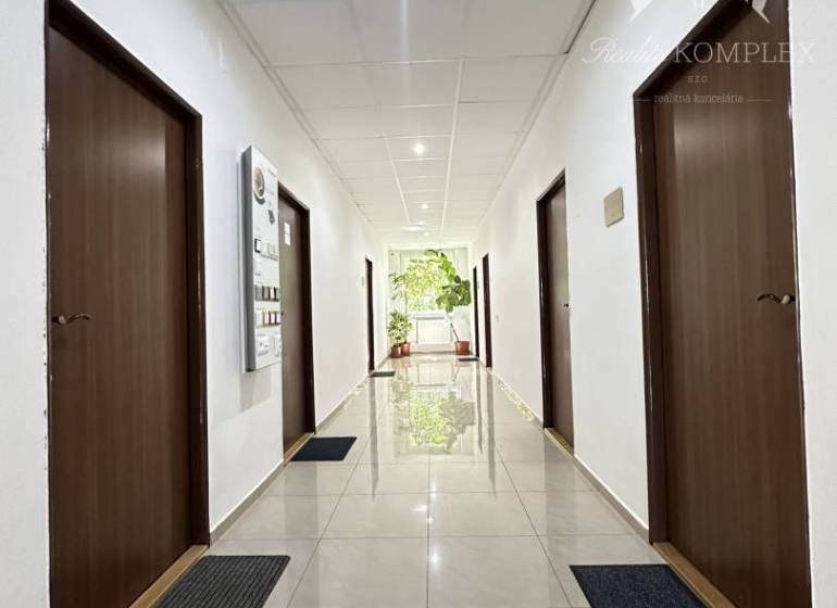A corridor of offices with brown doors and shiny white floor.