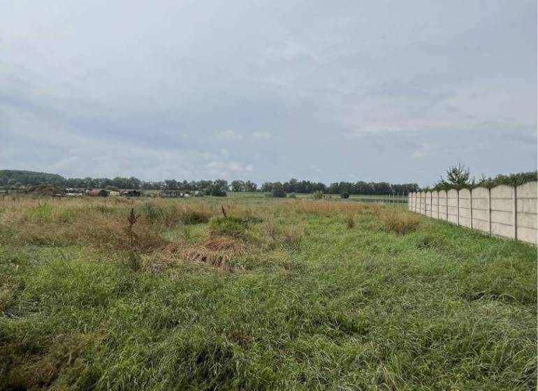 Residential plots in Iža with a view of the surrounding countryside and a fence.