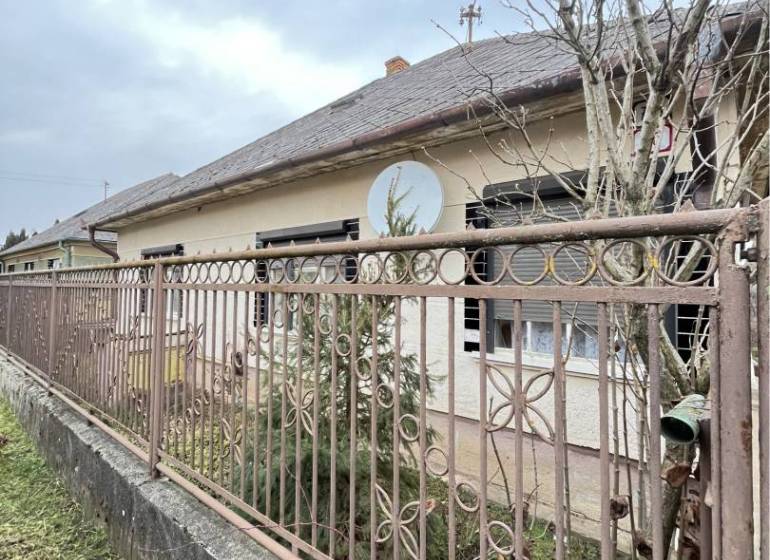 A family house in Strekov behind a metal fence, surrounded by trees and a peaceful environment.