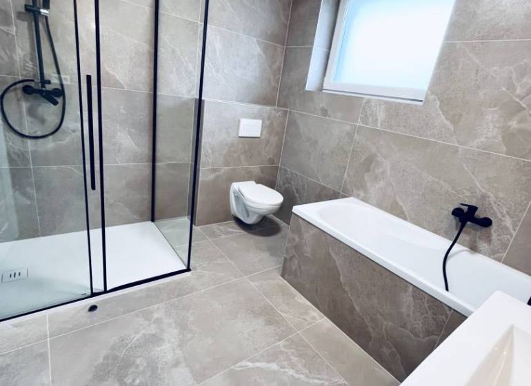 A bathroom in a family house with a glass-enclosed shower and light tiles.
