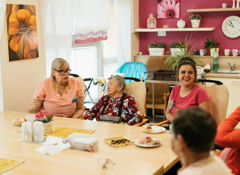 A group of people indoors discussing around a table with food and drinks.