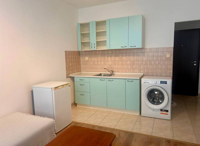 Studio apartment with kitchenette, washing machine, and refrigerator; floor with wood decor.