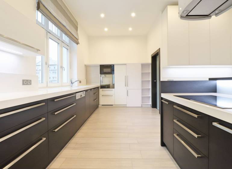 A kitchen in a 3-room apartment with a wooden decor floor and white cabinets.