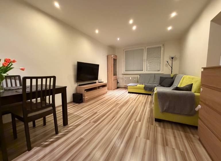 Living room with a sofa, dining table, and wood-patterned flooring in a 3-room apartment.