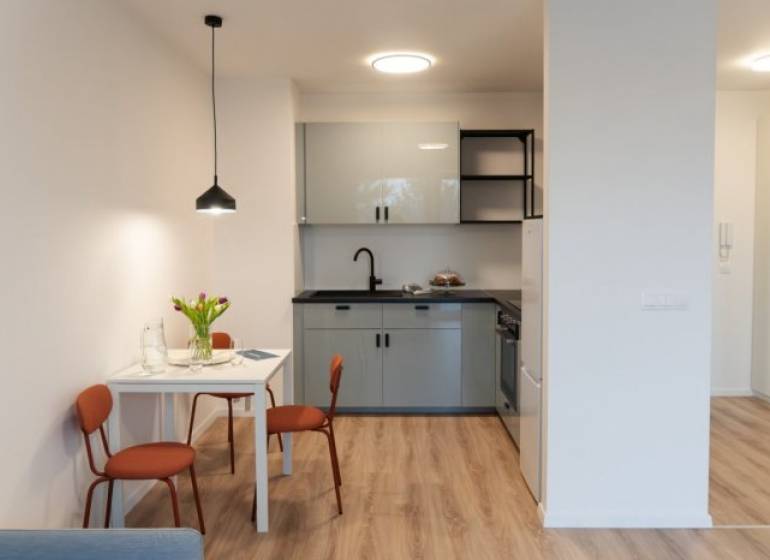 A studio apartment with a wooden decor floor, a dining table, and a kitchenette.