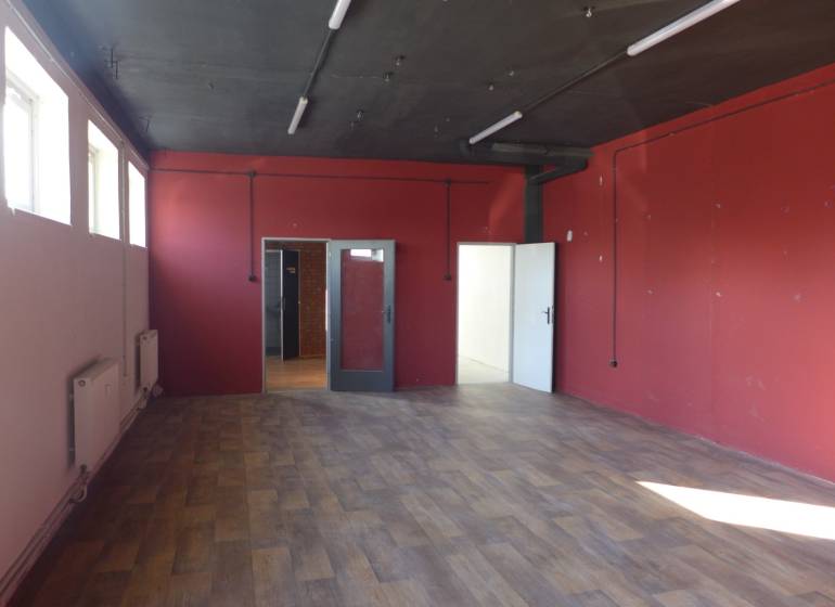 Red walls, wood-patterned floor, and windows in an industrial space of warehouses and halls.