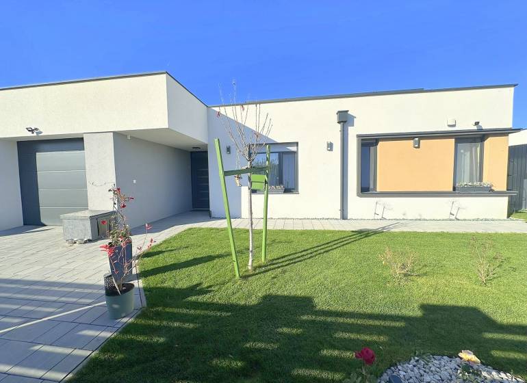 A family house in Mosonmagyaróvár with a green lawn, stone decor, and elegant flowers in pots.