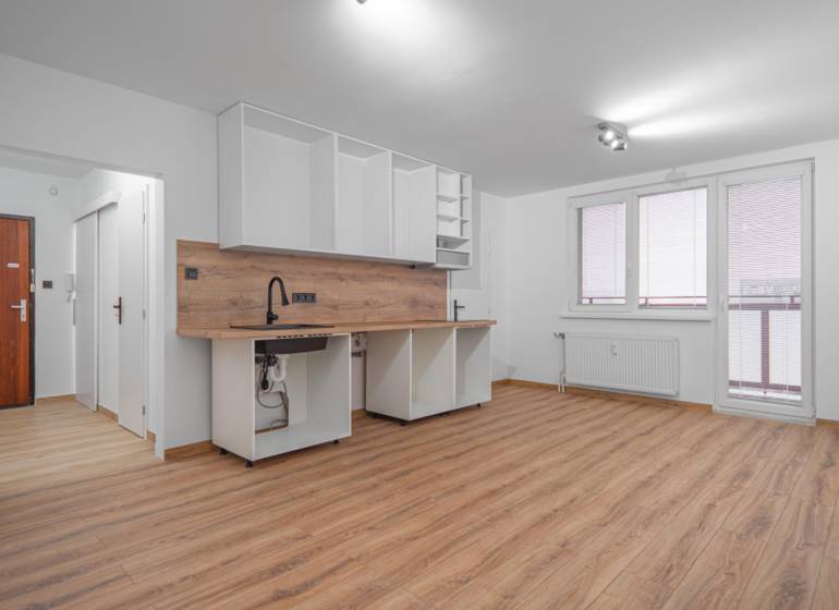 Kitchen unit in a studio apartment with white cabinets and a wood-patterned floor.