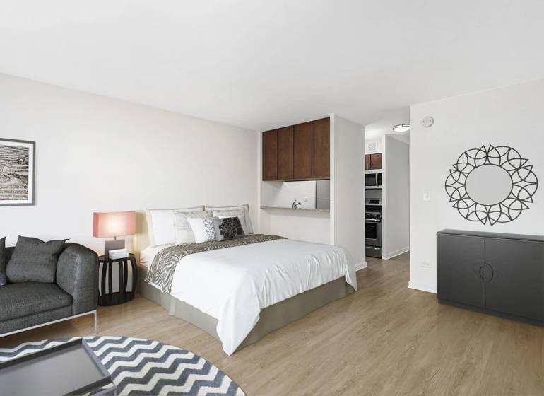 A one-room apartment with a bed, a sofa, and a wooden decor floor in a light interior.