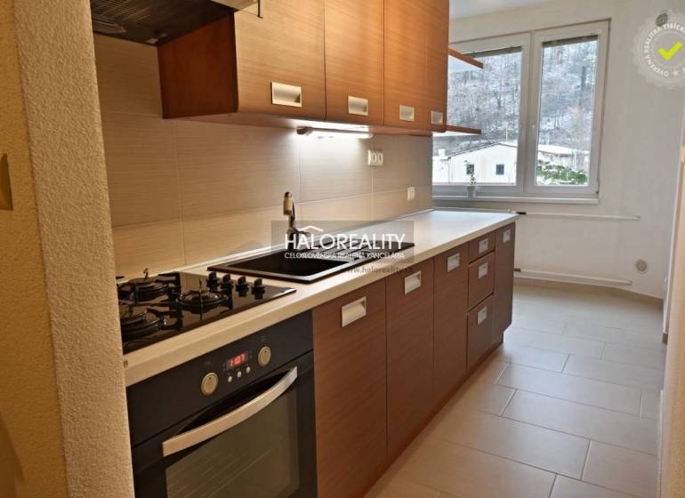 A kitchen in a 2-room apartment with a cooktop, oven, and a window with a view.
