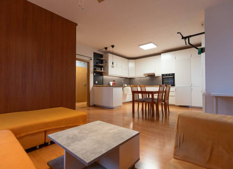 Interior of a 1-room apartment with a wooden decor floor, kitchen, and dining table.
