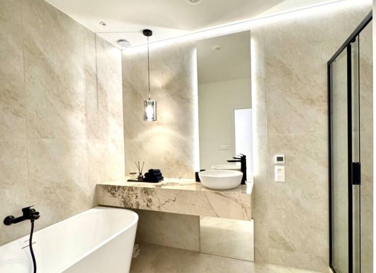 A bathroom with a freestanding bathtub in a 4-room apartment, with light tiles and a mirror.