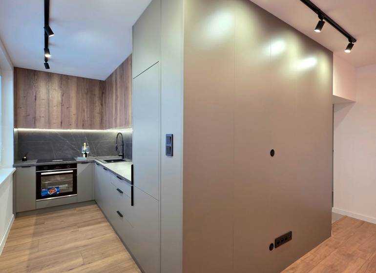 Kitchen area of a 3-room apartment with a wooden decor floor and ceiling track lighting.