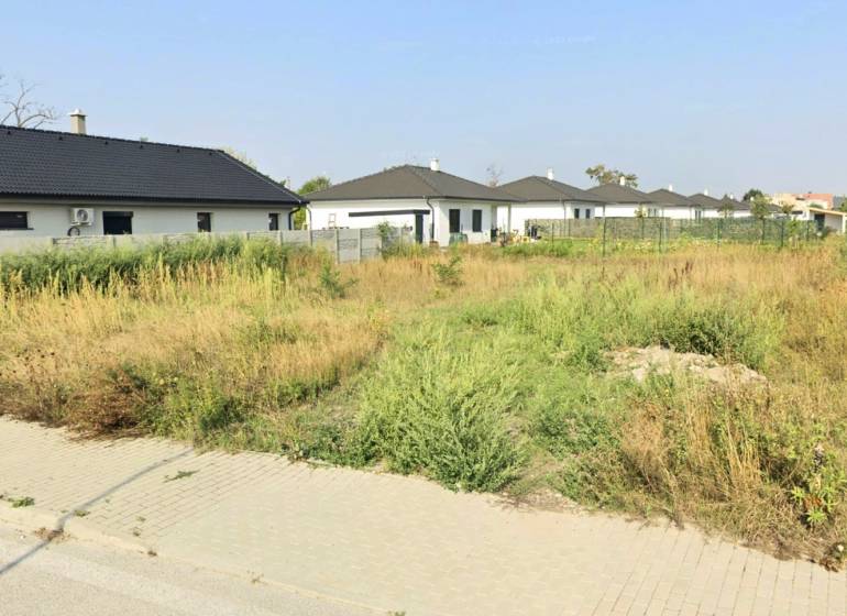A residential plot in Kvetoslavov on Bazová Street with greenery and surrounding houses.