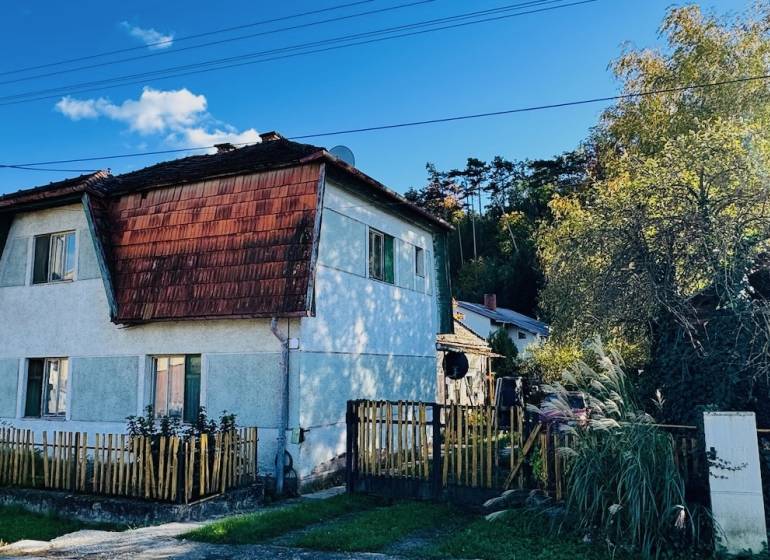 A family house in Brodzany with a wooden fence and a sloped roof, surrounded by greenery.