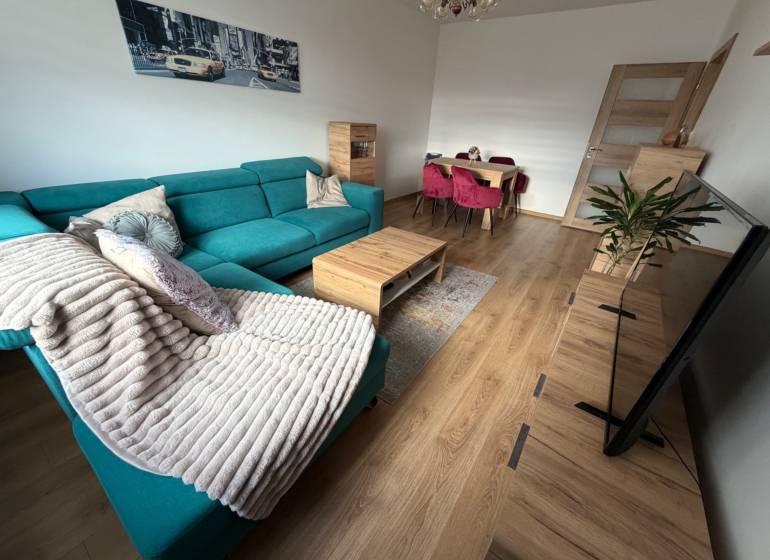 Living room of a 4-room apartment with a turquoise sofa, wooden decor flooring, and a dining table.