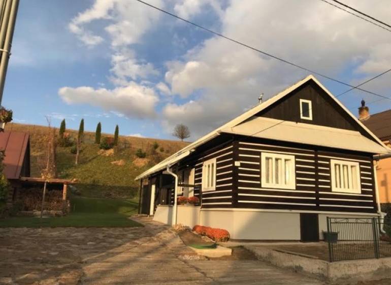 A cottage in Legnava with wooden cladding and a paved courtyard, surrounded by nature and hills.