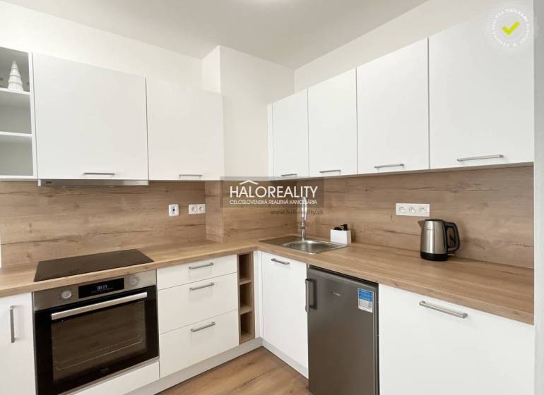 A kitchen in a studio apartment with a wood-patterned floor and white cabinets.