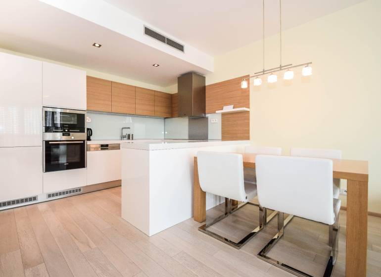 A kitchen with white cabinets, a dining table, and a wooden decor floor in a 3-room apartment.