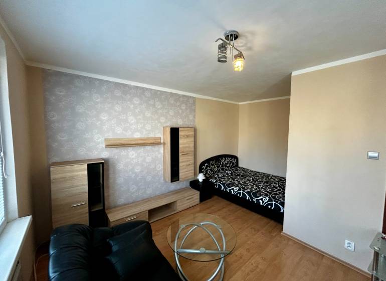 A room in a one-room apartment with a bed, a black armchair, and a floor with a wood decor.