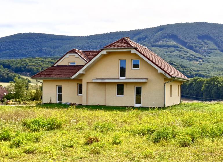 A family house in Buková with a red roof surrounded by green hills in the background.