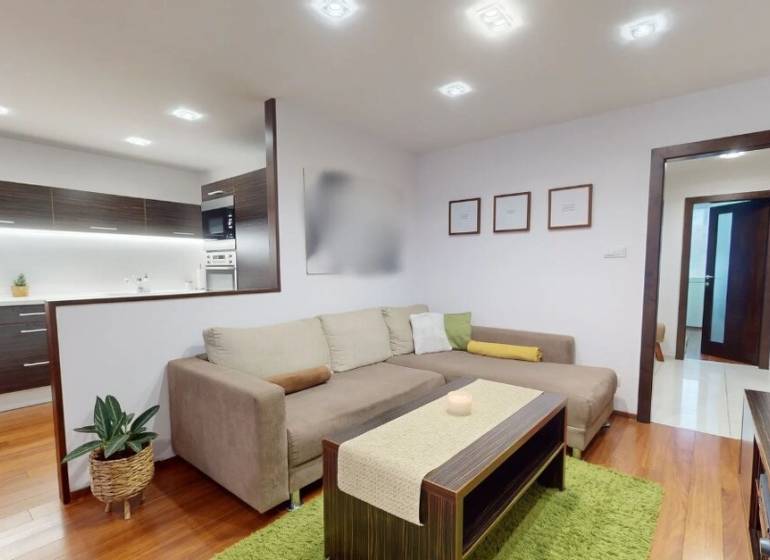Living room in a three-room apartment with a wood-patterned floor and a comfortable sofa set.