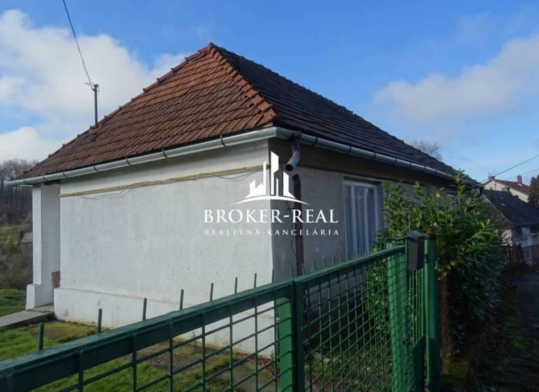 A family house in Rudabánya with a white facade and a sloped roof behind a green fence.