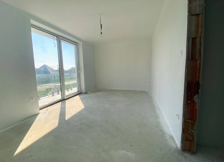 An unfurnished room with a large window, cement floor in a family house.