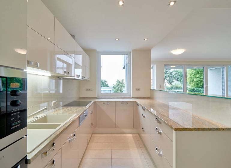 A kitchen in a 3-room apartment with a large window, white cabinets, and a glossy countertop.