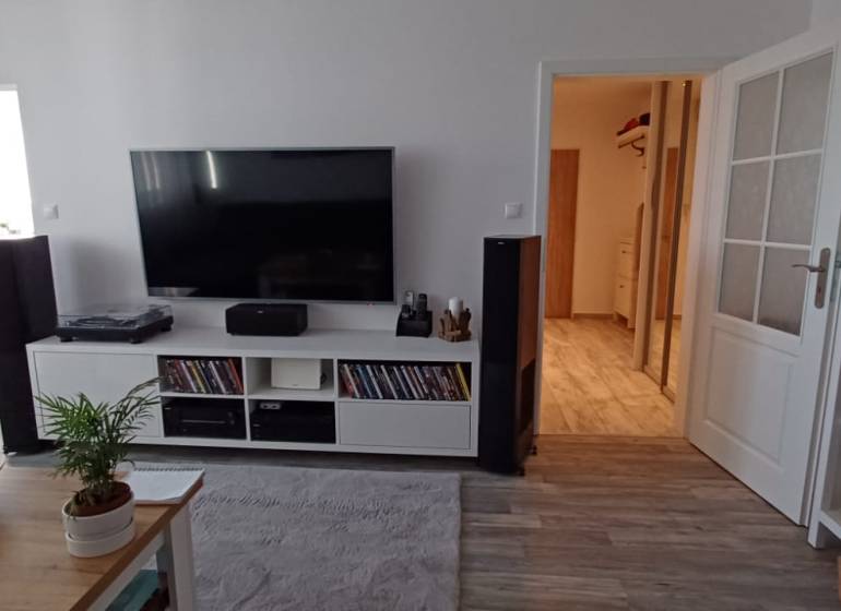 Living room with a coffee table, television, and bookshelf in a 3-room apartment with a wood-patterned floor.