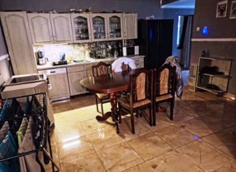 A kitchen in a family house with ceramic tiles, wooden cabinets, and a dining table.