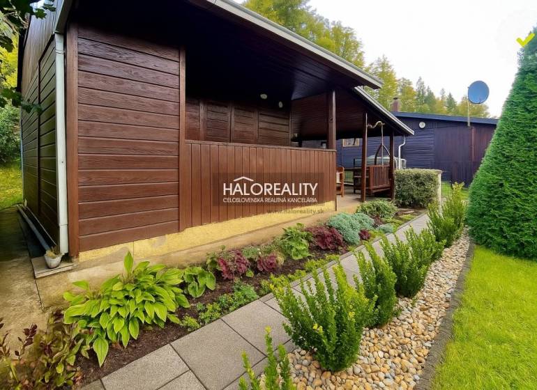 A wooden cottage in the gardens in Bytča, surrounded by well-maintained greenery and a path made of tiles.