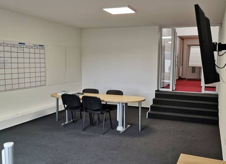 Offices with a conference table, chairs, a board, and a TV on the wall.