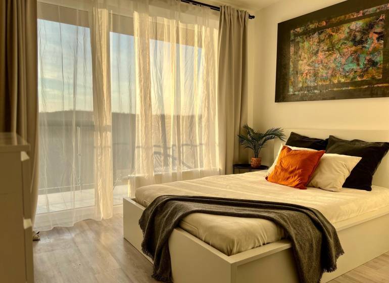 Bedroom with a bed, painting, and curtains in a studio apartment with wood-patterned flooring.